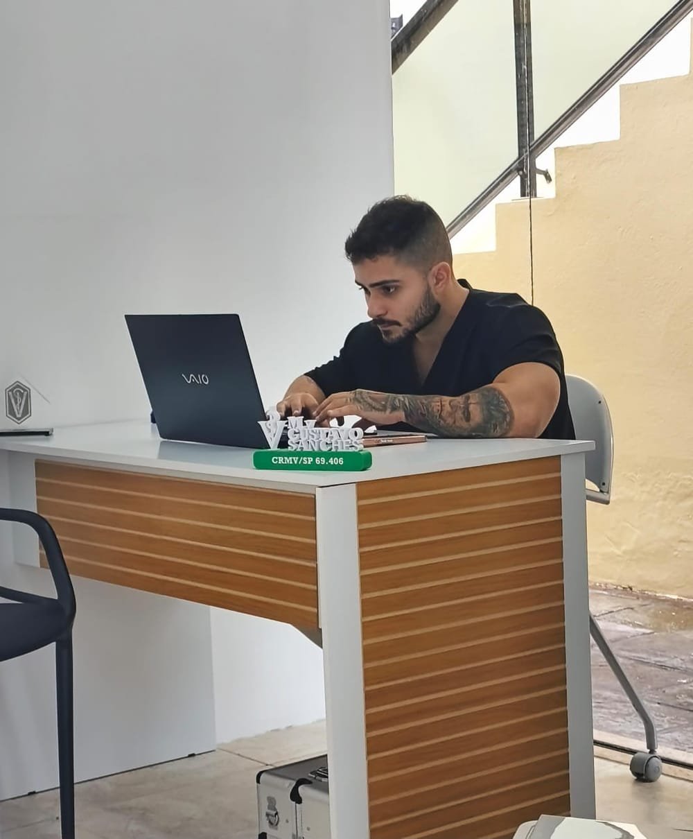 Veterinário trabalhando no consultório da IlhaVet, com a placa do CRMV sobre a mesa